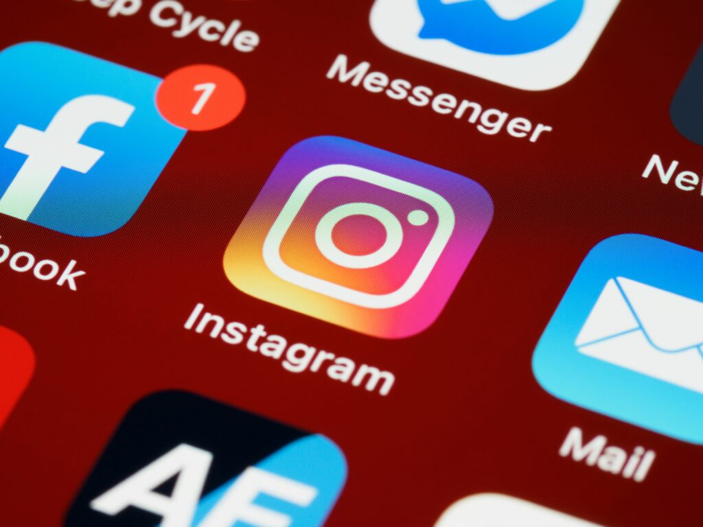 Close-up of a mobile phone screen showing various app icons, including Instagram, Facebook with a notification badge, Messenger, and a mail app. The Instagram app is in focus.